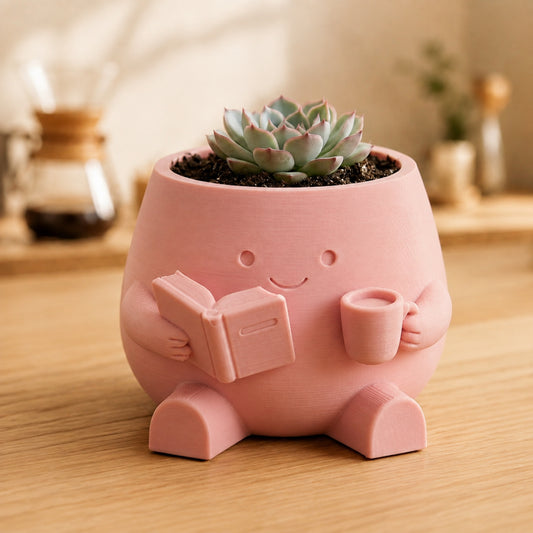 Vaso amiguinho segurando um livro aberto e uma xícara, na cor rosa